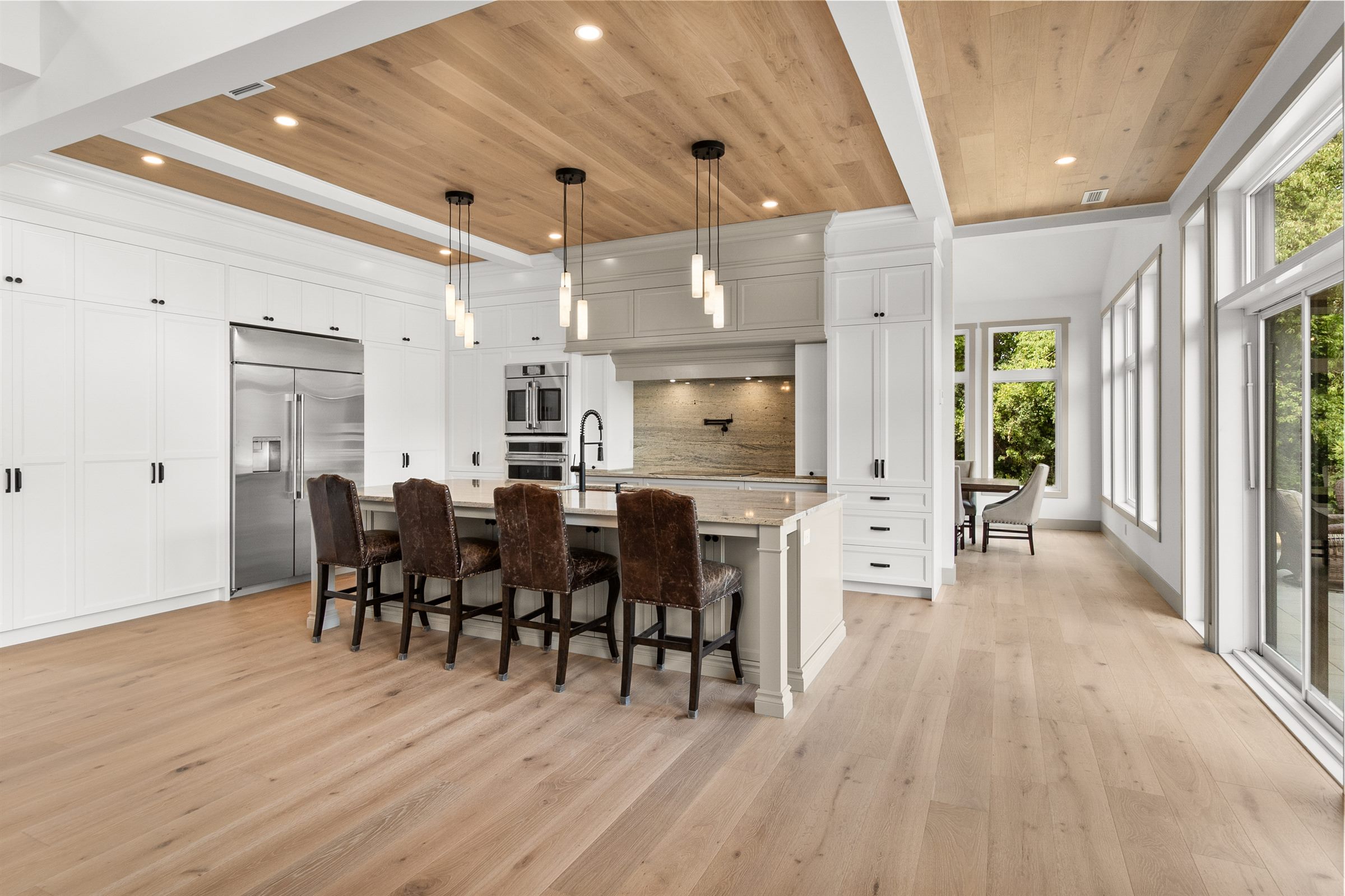 Grande cuisine blanche sur mesure : îlot avec quatre tabourets, plafond de bois et grandes fenêtres