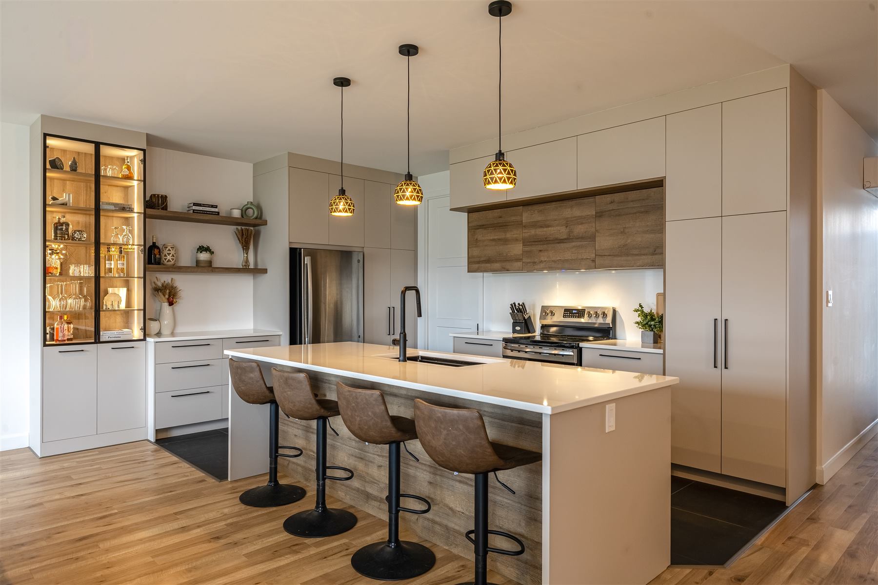 La Vitrine : Armoires taupe pleine hauteur, garde-manger vitré et étagère ouverte en noyer, comptoir de quartz blanc