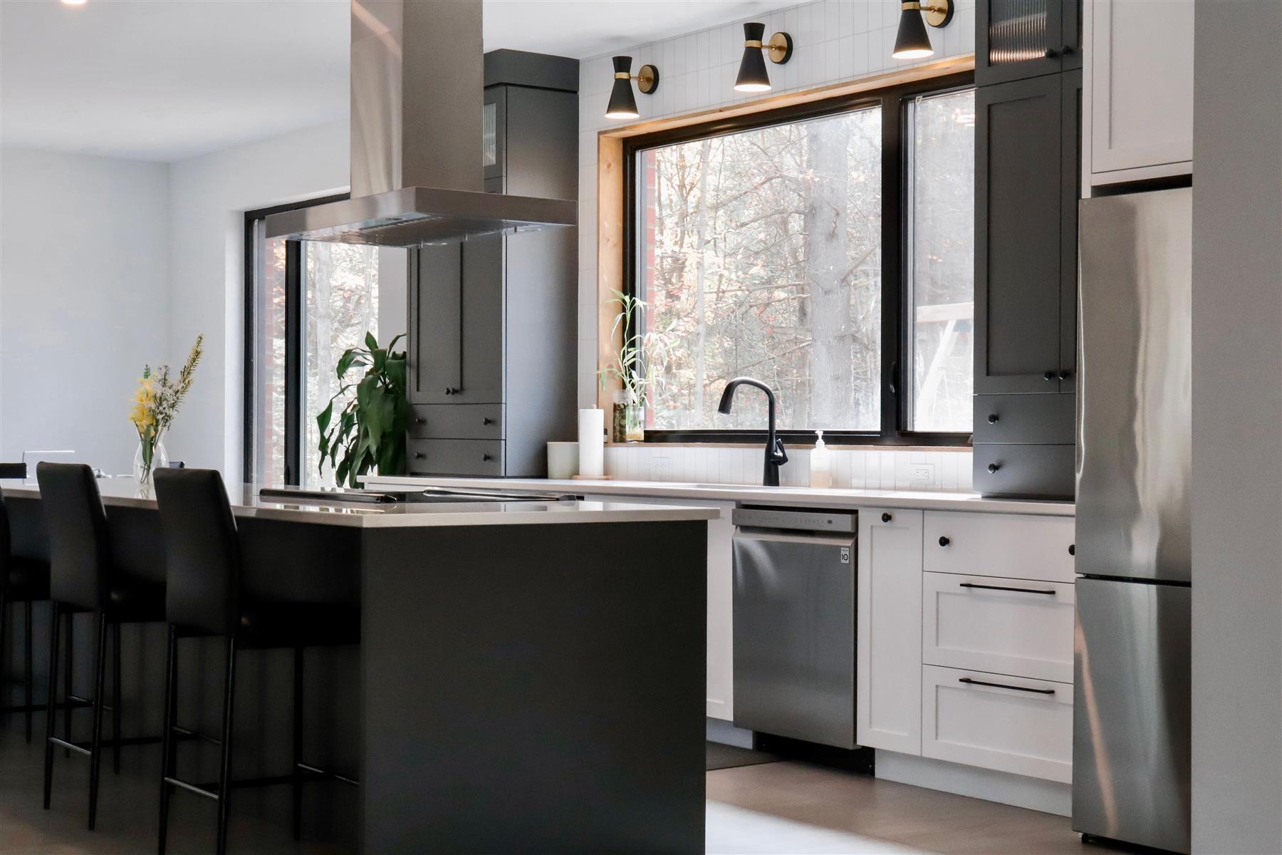 L’Anthracite : Armoires grises et noir mat, hotte intégrée et comptoir de quartz clair, sous une fenêtre pleine hauteur au-dessus de l'évier