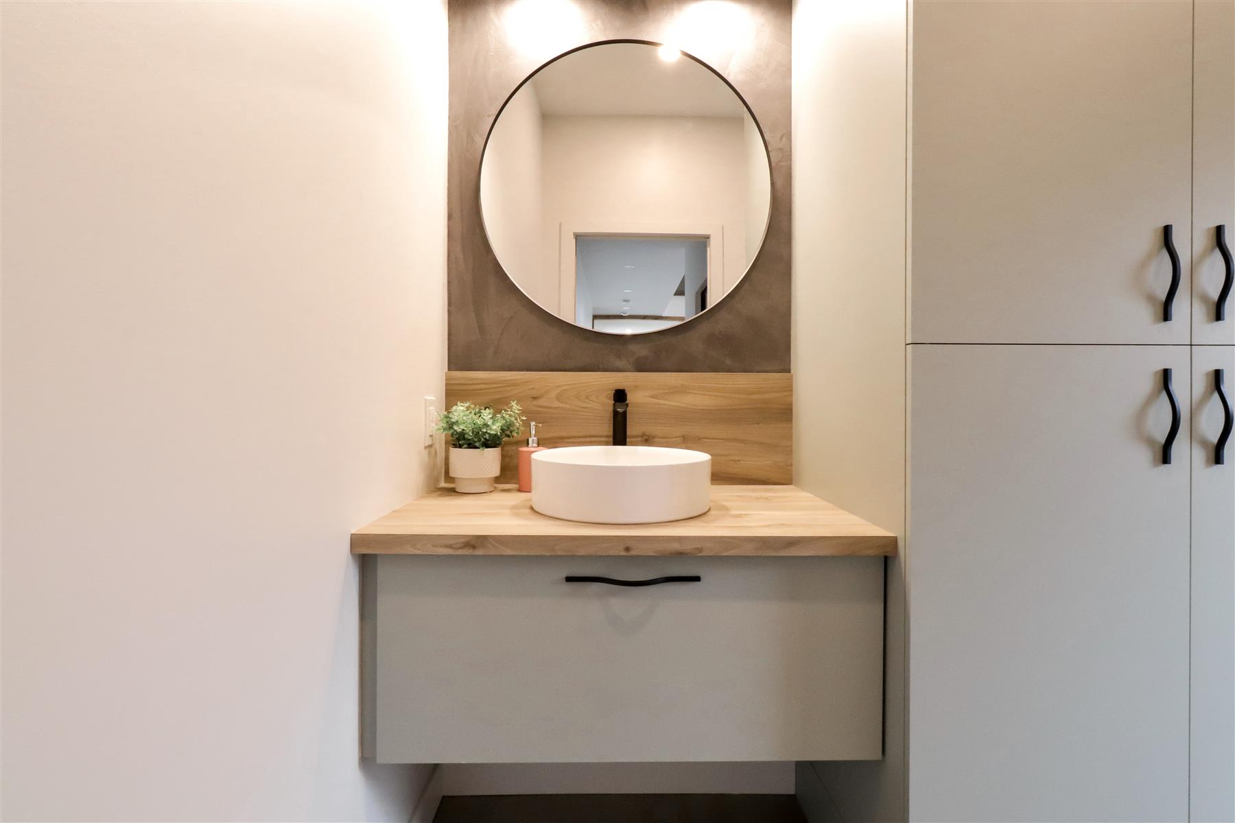 La Pleine Lune : Vanité flottante sur mur enduit foncé, dosseret en bois et armoire de rangement pleine hauteur